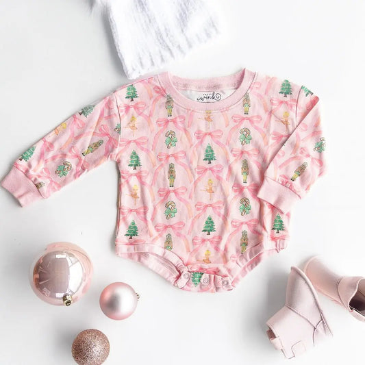 Pink romper with pink bows, green trees, and nutcrackers.