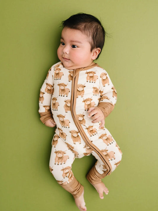 Baby wearing an ivory bamboo convertible sleeper with mini highland cow print.